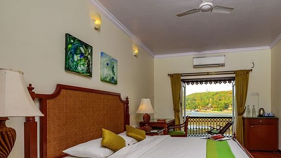 A double bed with painting hung above and balcony in the centre inside Coral - River View room at neemrana s three waters