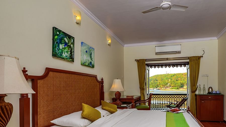 A double bed with painting hung above and balcony in the centre inside Coral - River View room at neemrana s three waters