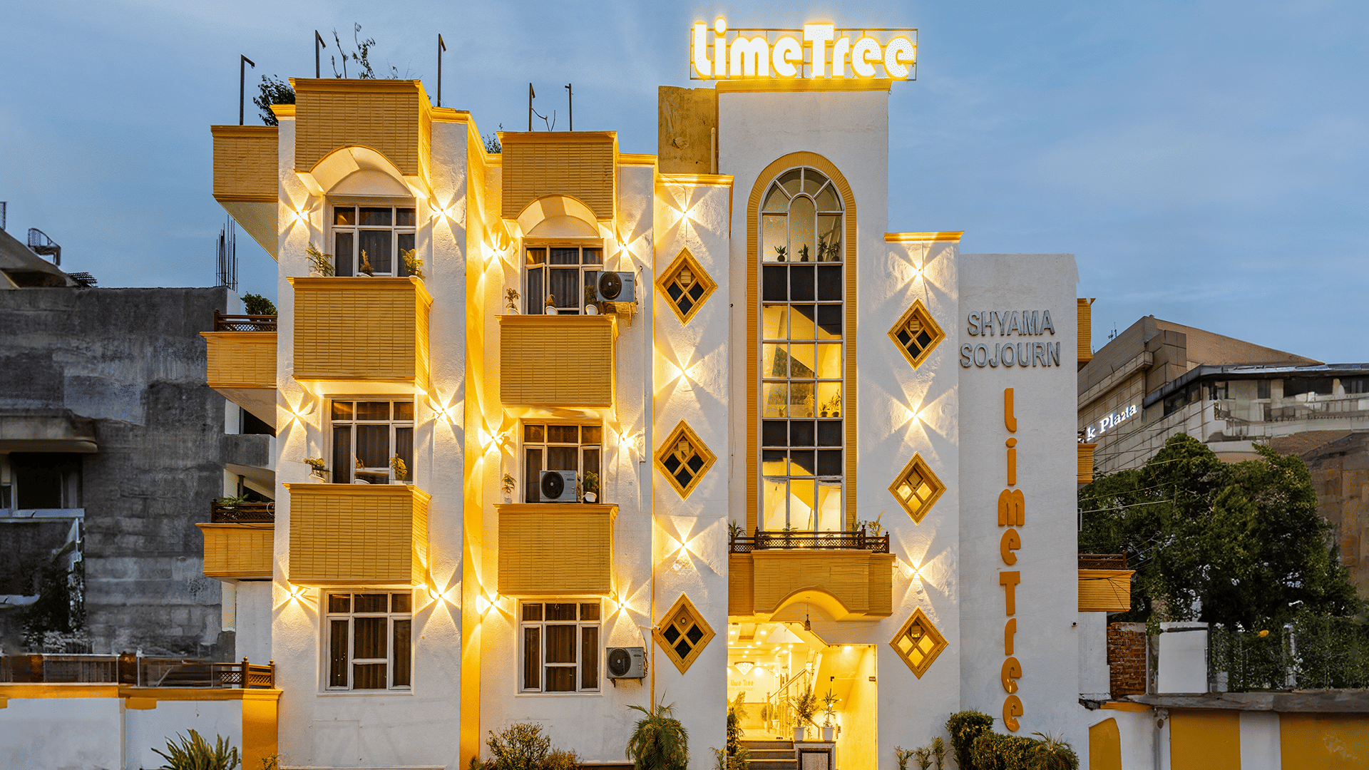 Ornate multiple storey building exterior of Lime Tree Hotels & Service Apartment Private Limited illuminated at dusk.