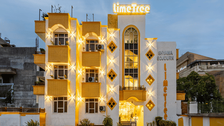 Ornate multiple storey building exterior of Lime Tree Hotels & Service Apartment Private Limited illuminated at dusk.