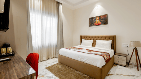 Bedroom of Lime Tree Hotels & Service Apartment Private Limited featuring a wooden headboard, a red accent chair, and curtained windows.