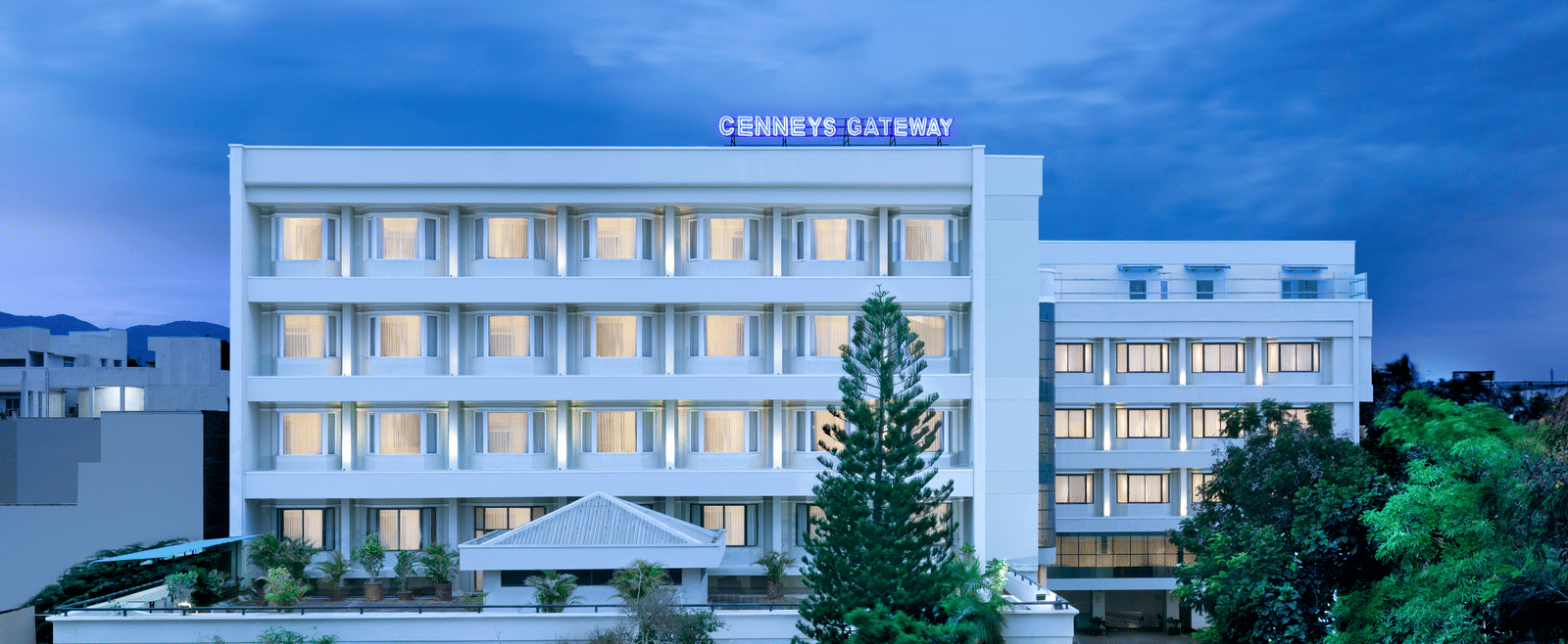 A facade view of Cenneys Gateway against the sky, surrounded by trees and plants in the front.
