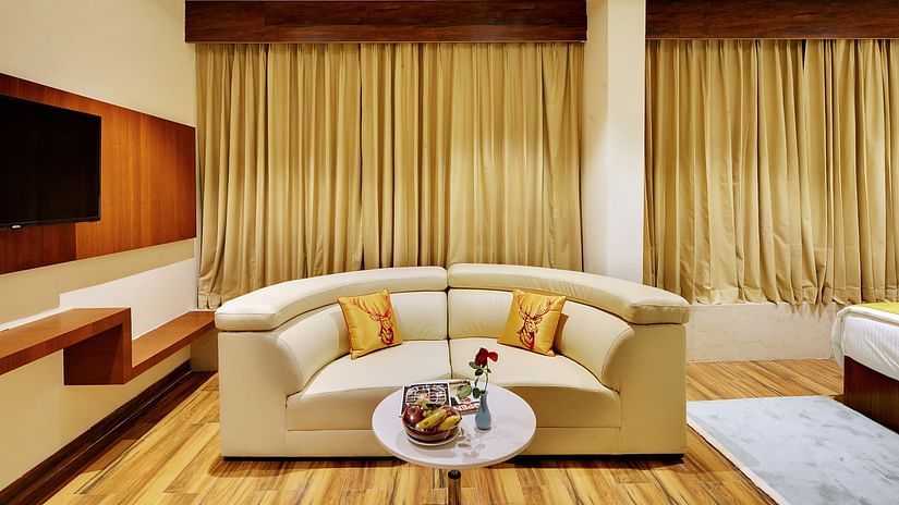 An image of a sofa with centre table and a flat V screen next to it at Mastiff Select Hotel Gulbarga