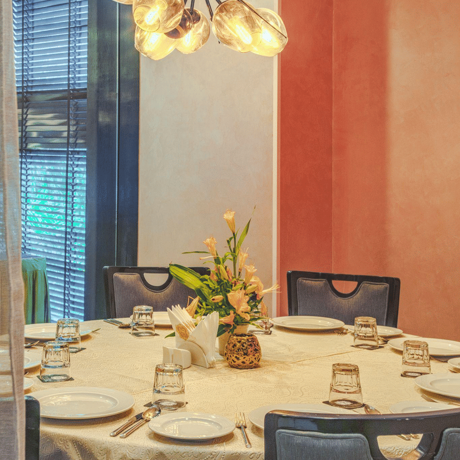 Elegant round dining table with a white tablecloth, set with fine dinnerware under a modern chandelier.