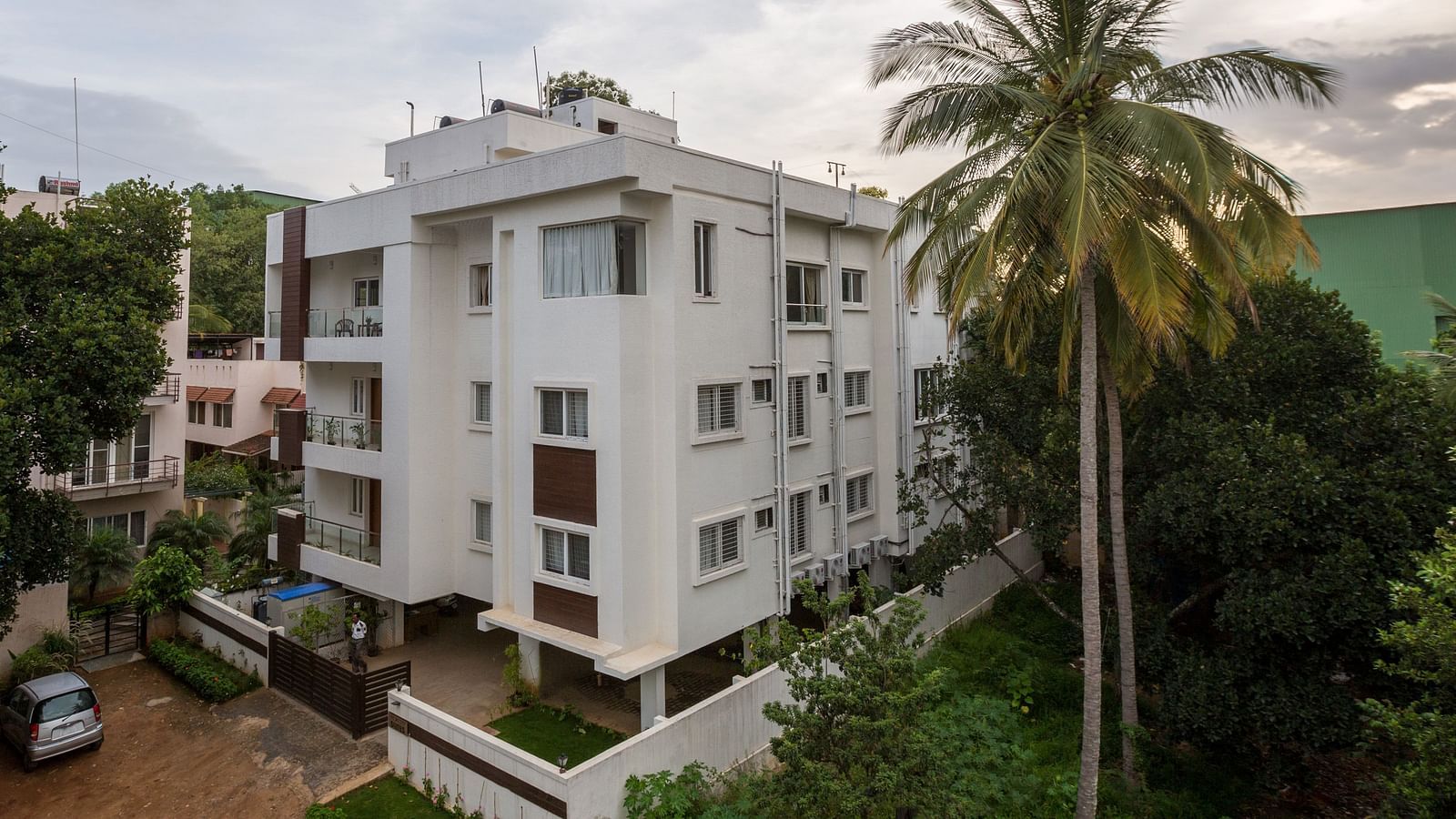 A light-coloured building exterior surrounded by green trees under a bright sky - Sanctum Suites BEL Road, Bangalore