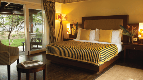 An overview of a bedroom at The Serai Kabini with a king size bed, chairs, side tables and lamps .
