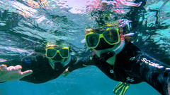 Two people wearing snorkelling gear are pictured underwater, smiling at the camera.