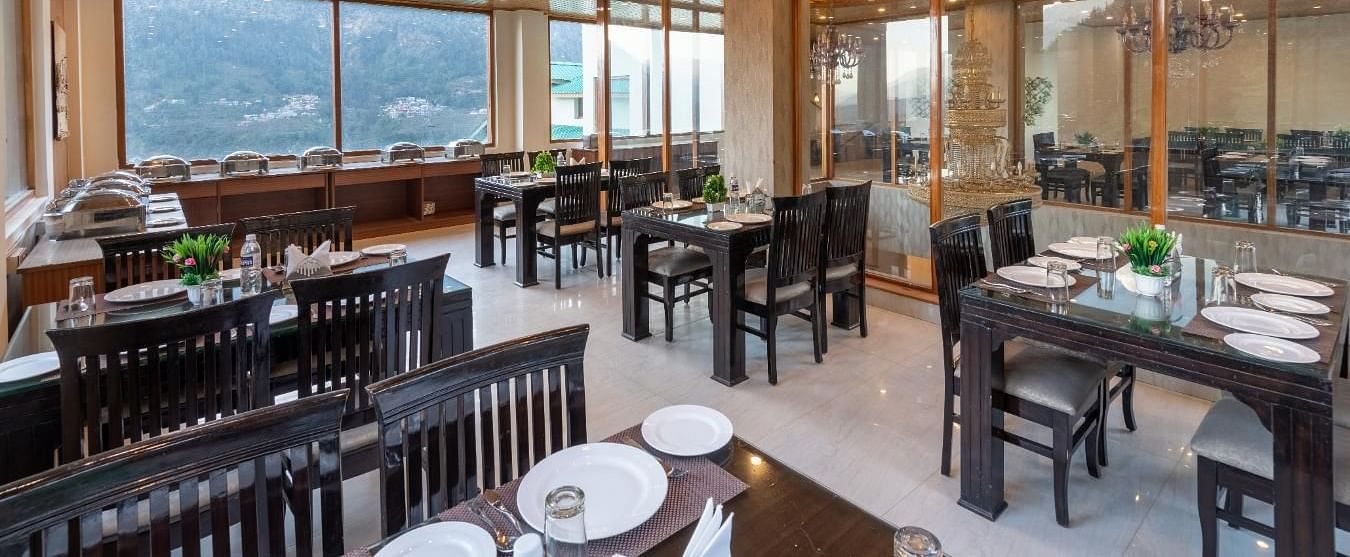The image showcases a contemporary restaurant with large windows framing stunning mountain views  | DLS Serenity Resort and Spa