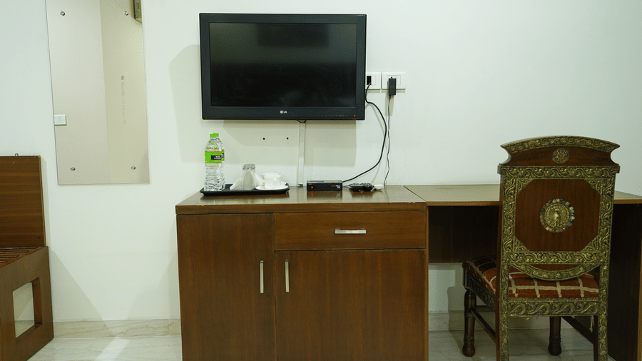 Guest room with a wall-mounted LG TV, a wood console holding a water bottle and cups, a mirror, and a carved chair.