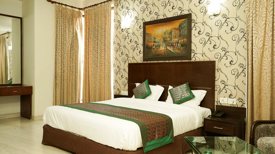 Bedroom of Lime Tree Hotels & Service Apartment Private Limited featuring a dark wooden headboard, green cushions, and framed wall art.