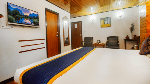 An image of a bedroom featuring a bed, chairs, a table with tea and coffee maker, and a mirror attached on the wall at Central Hill Resort, Gangtok