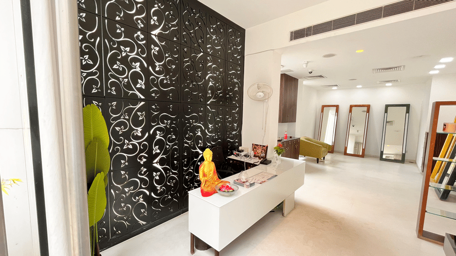 A bright and stylish spa reception area with a modern white counter, decorative black patterned wall and indoor plant atSprings Hotel & Spa, Bangalore