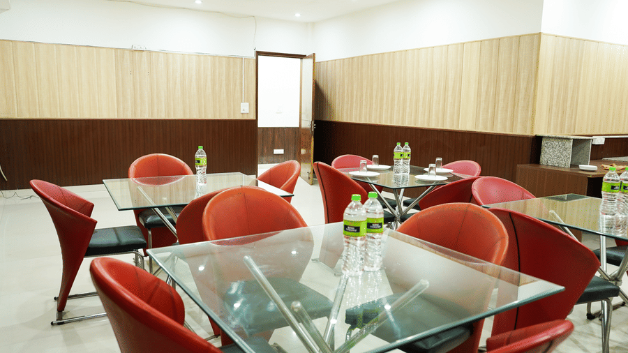 Dining area with red chairs and glass-topped tables set with water bottles, plates, and folded cutlery.