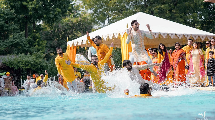 Joyful haldi ceremony with guests celebrating in a poolside setting.
