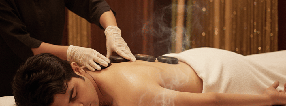 Therapist giving a relaxing back massage to a woman in a warm, candle-lit spa room at Bamboo Saa Sunrrise Wedding & Wellness Resort, Jaipur.