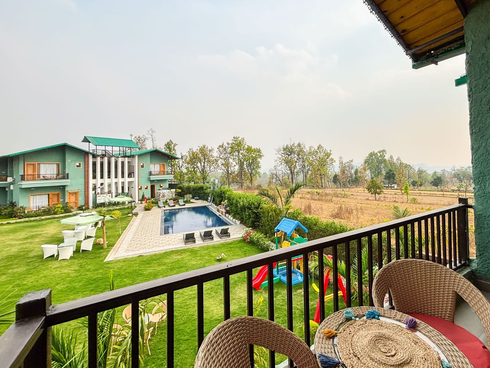 A wide angle shot of a balcony overlooking a bright lawn area under a clear blue sky in the background at Corbett Nirvana Resort.