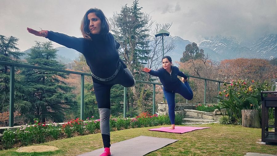  A woman performing a yoga stretch on an outdoor mat, dressed in sportswear, with a scenic view of mountains and a cloudy sky in the background.
