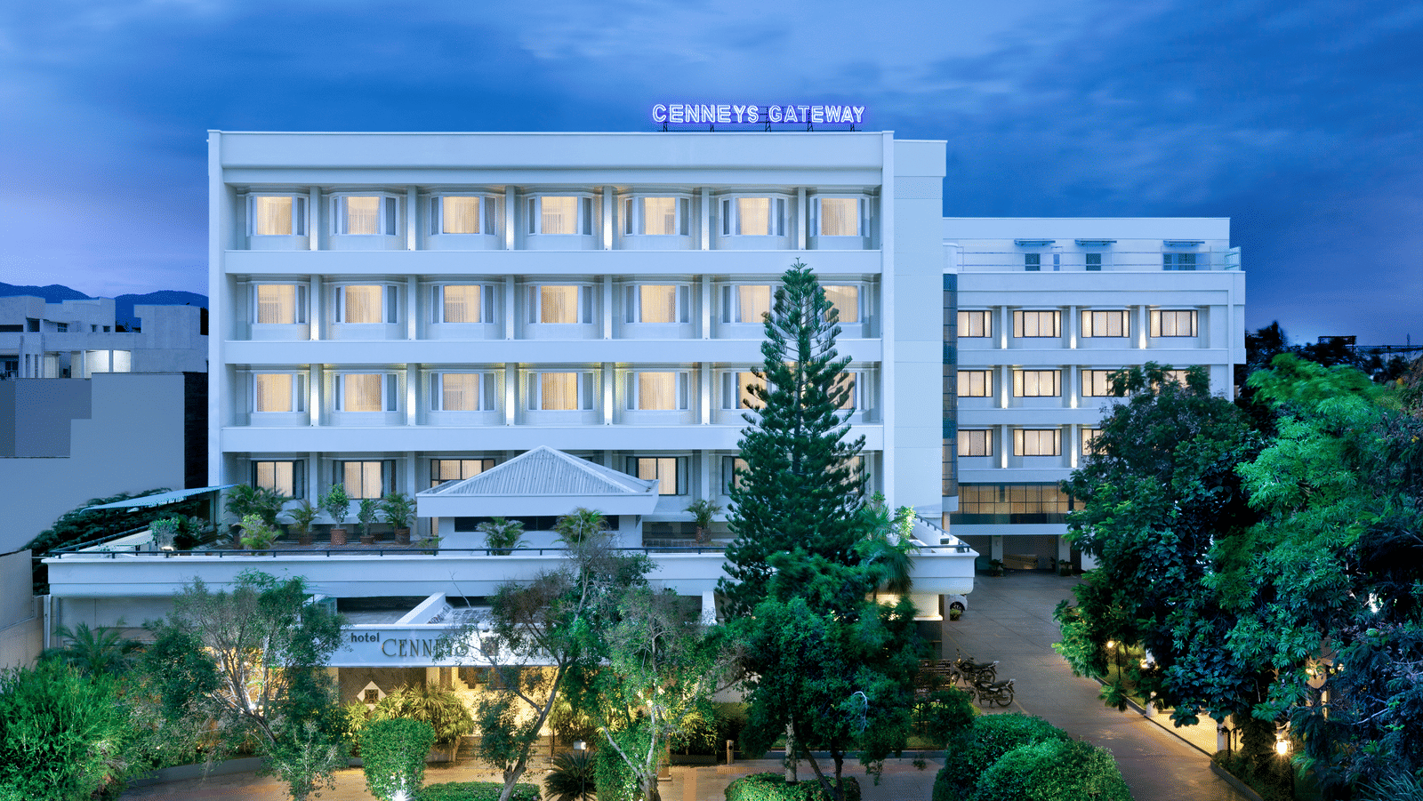 A facade view of Cenneys Gateway against the sky, surrounded by trees and plants in the front.