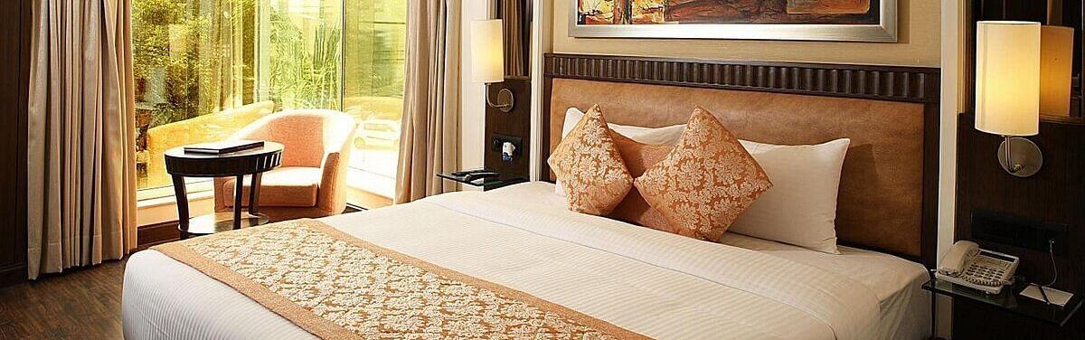 Executive Room with a double bed, bedside table with a lamp on top, cushioned seating with a table in front, and a window behind at Inde Signature Tower, Gurgaon