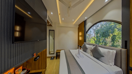 The Standard Room at Lords Inn Vadodara, showcasing a bed facing a wall-mounted television, a large window with an outdoor view, and ceiling lighting.