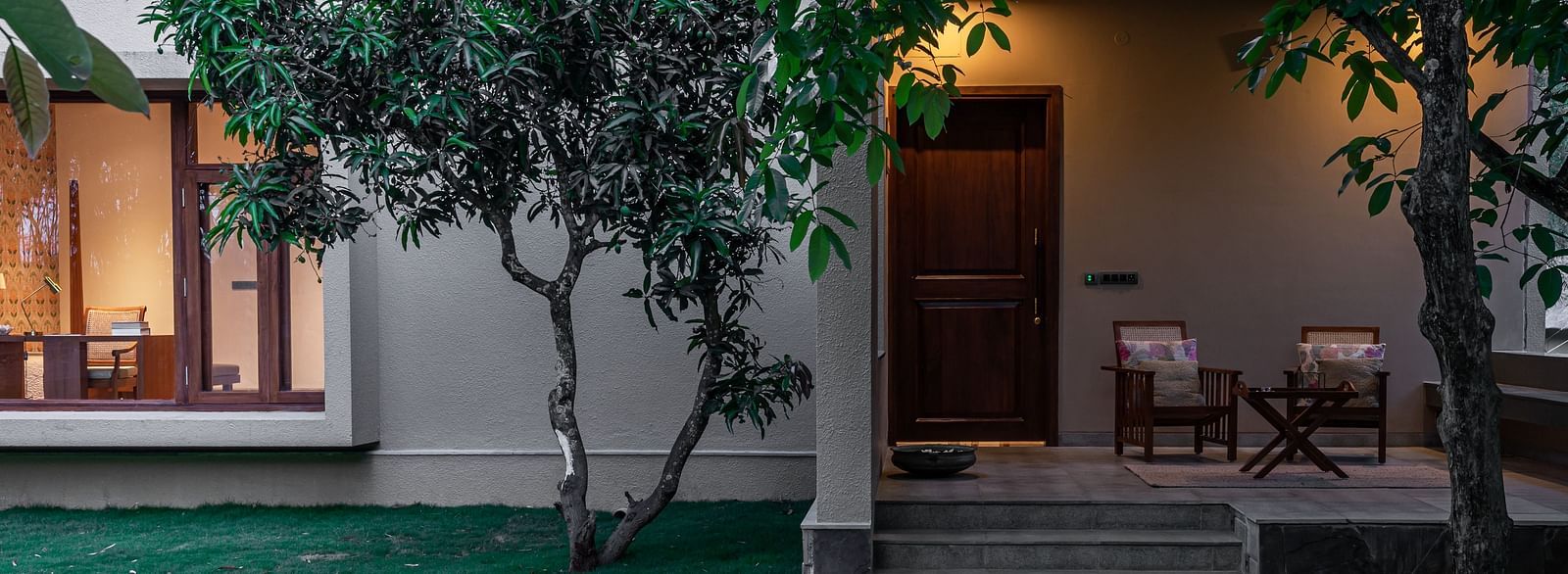 Exterior of a building with lit windows, trees, and a stone pathway at dusk at Shreyas Retreat