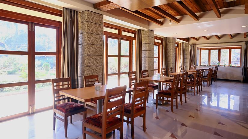 Bright, airy restaurant interior with wooden tables and chairs, large windows, and natural light at Hotel Kohinoor Highway, Dapoli