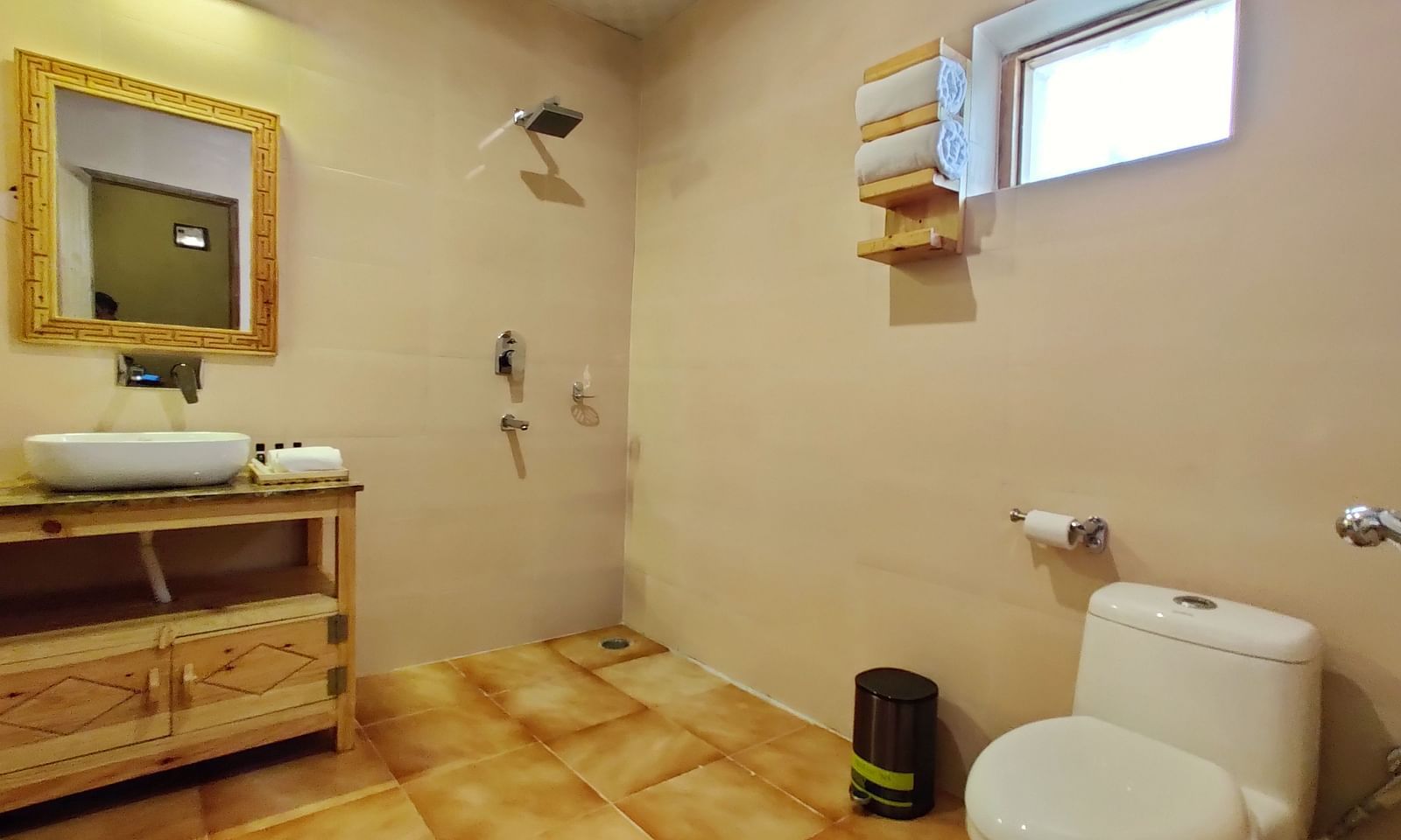 A bathroom at Standard Cottage with a toilet, a sink, a mirror, and beige tiles at White Sands Resort, Ladakh.