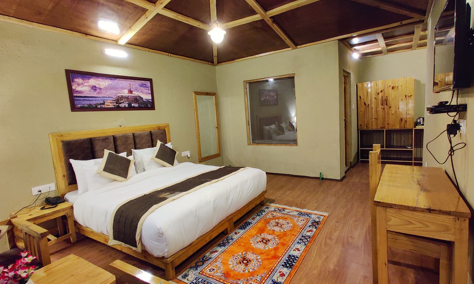 Premium Cottage at White Sands Resort, Ladakh with a king size bed, wooden furniture, and a patterned rug.