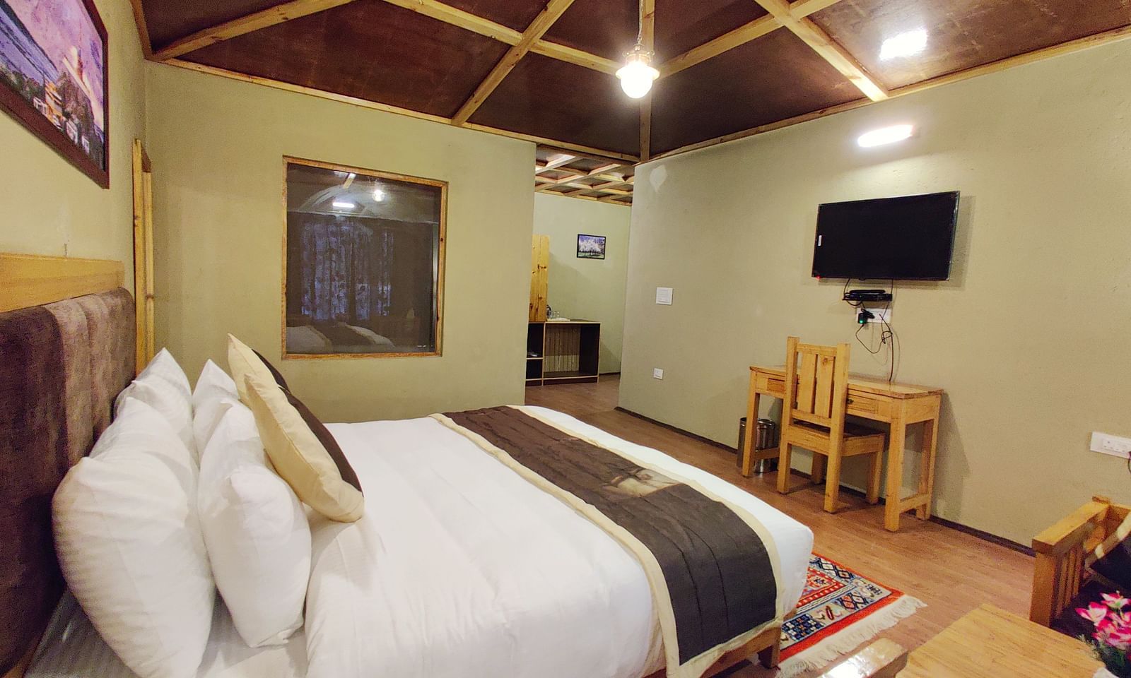 A close-up of a king size bed in Premium Cottage at White Sands Resort, Ladakh, highlighting the headboard, pillows, and bedside table.
