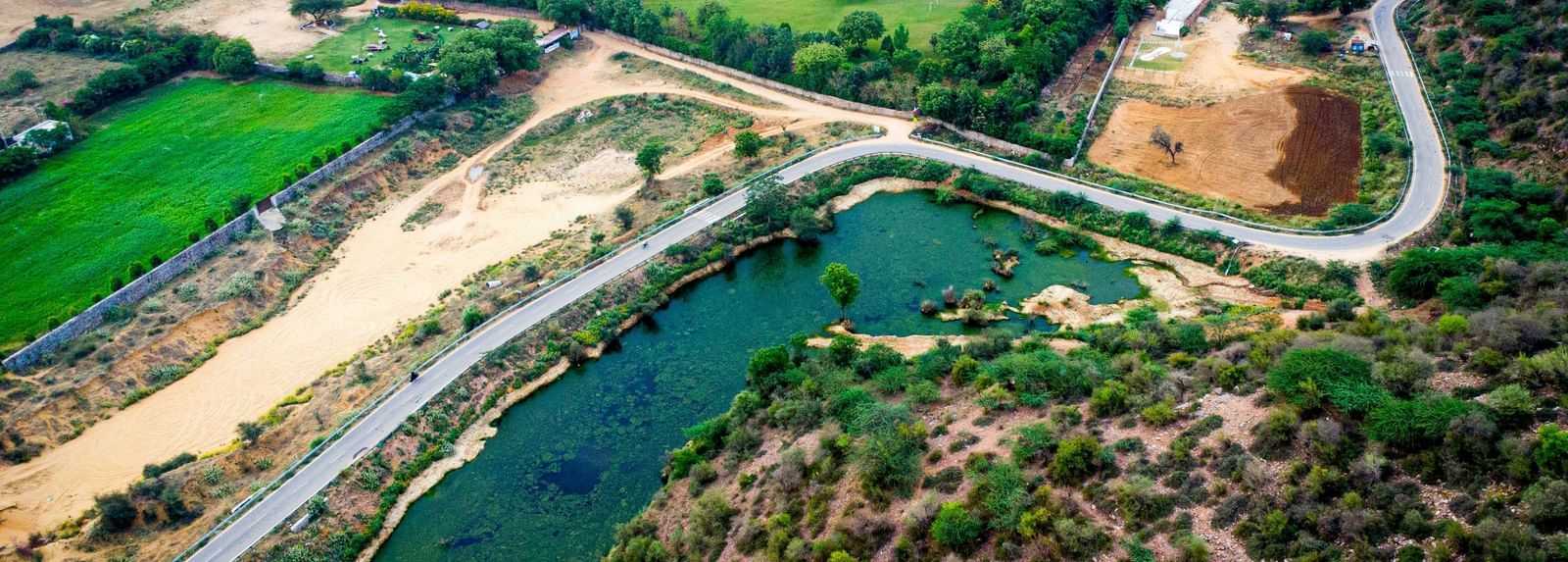 An aerial view of the Aravali Hills with a road, a small lake and greenery in view.