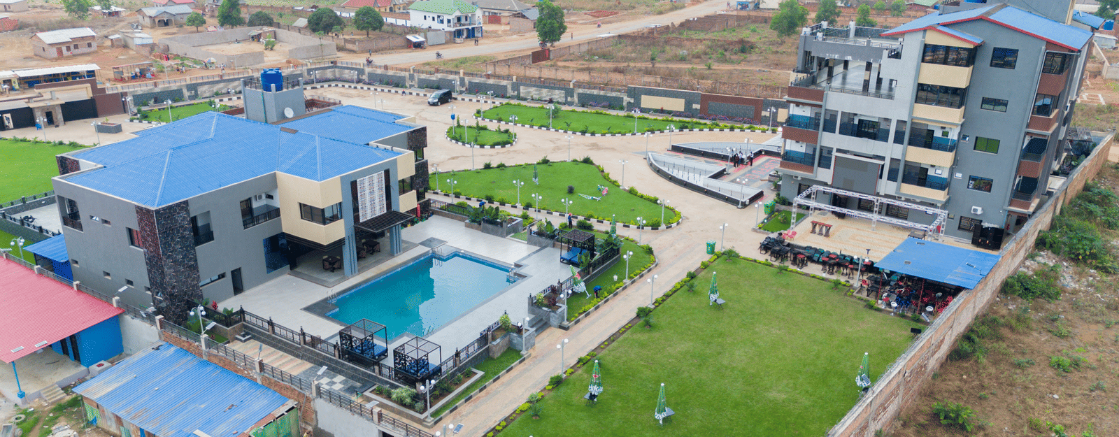 Wider aerial view of a building complex with a swimming pool, showing the surrounding neighbourhood - Luffu Club