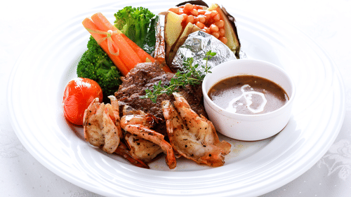 A plate with grilled meat, vegetables, and a dipping sauce.