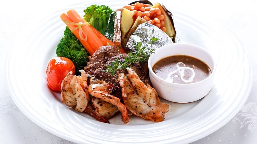 A plate with grilled meat, vegetables, and a dipping sauce.