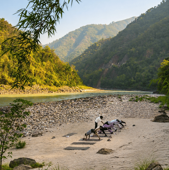 A group of people indulging into an early morning yoga session by the Ganges, with a beautiful backdrop of the hills.