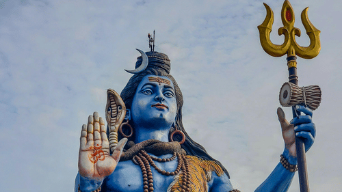 A large, blue statue of Lord Shiva seated with a trident.