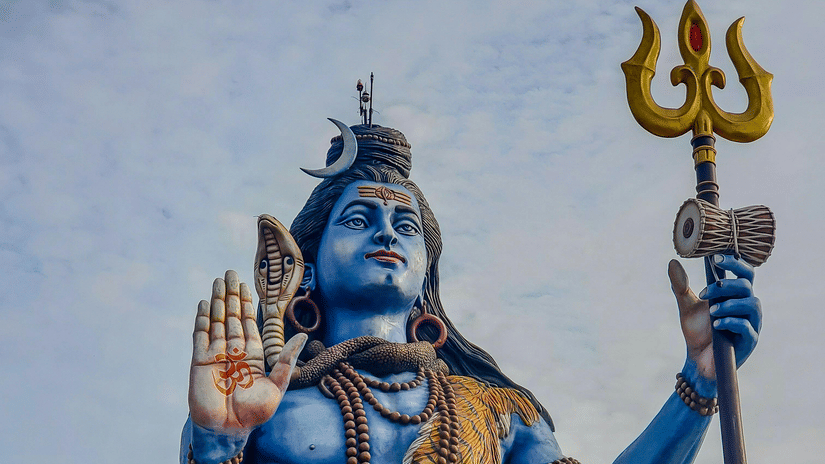 A large, blue statue of Lord Shiva seated with a trident.