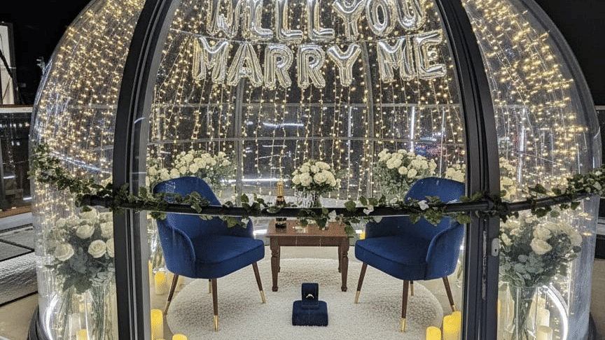 A round, dome-shaped dining booth or structure with glass panels and a detailed metallic framework, containing a small dining table and chairs | Pride Elite Chhatrapati Sambhajinagar