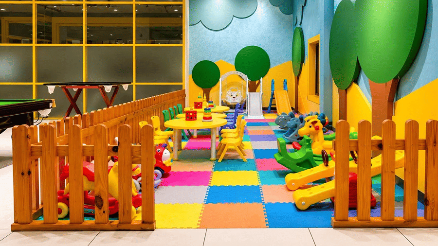 A play area at Hotel Sonar Bangla, Mayapur, featuring a wooden fence enclosure, small seating arrangements, and rocking toys.