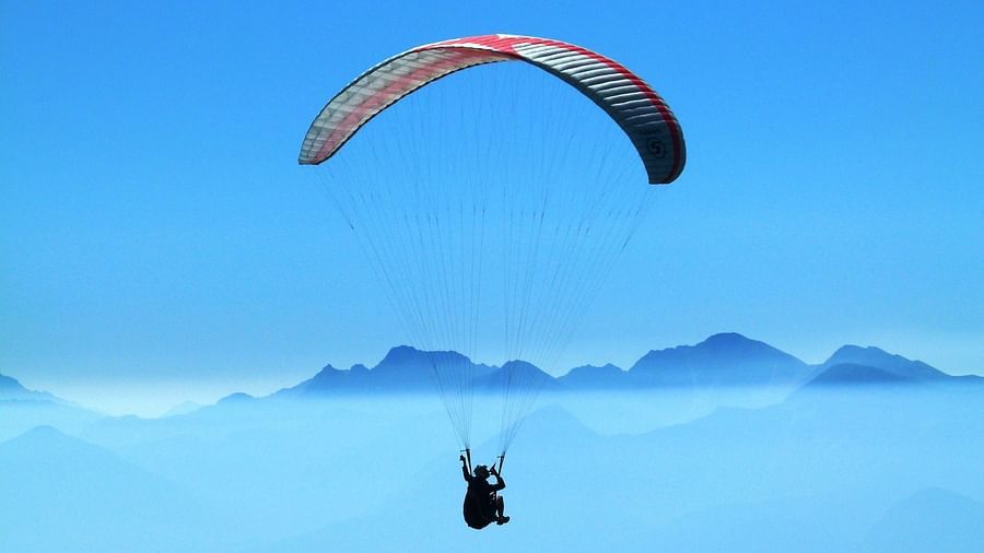 A person soaring through the sky while paragliding, experiencing the thrill of flight against a clear blue backdrop.