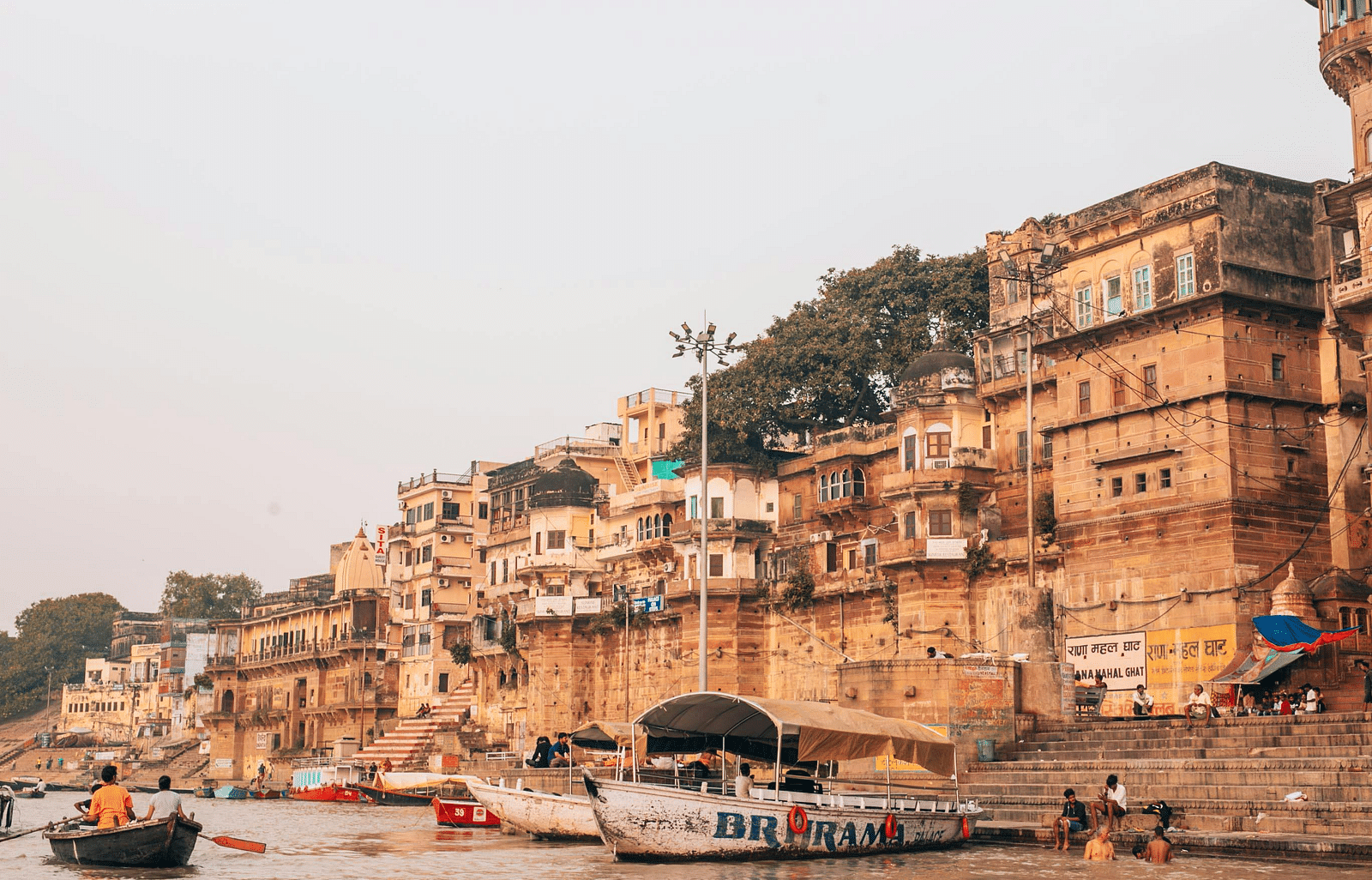 A daytime view of Varanasi featuring several boats at Rana Mahal Ghat, surrounded by buildings.