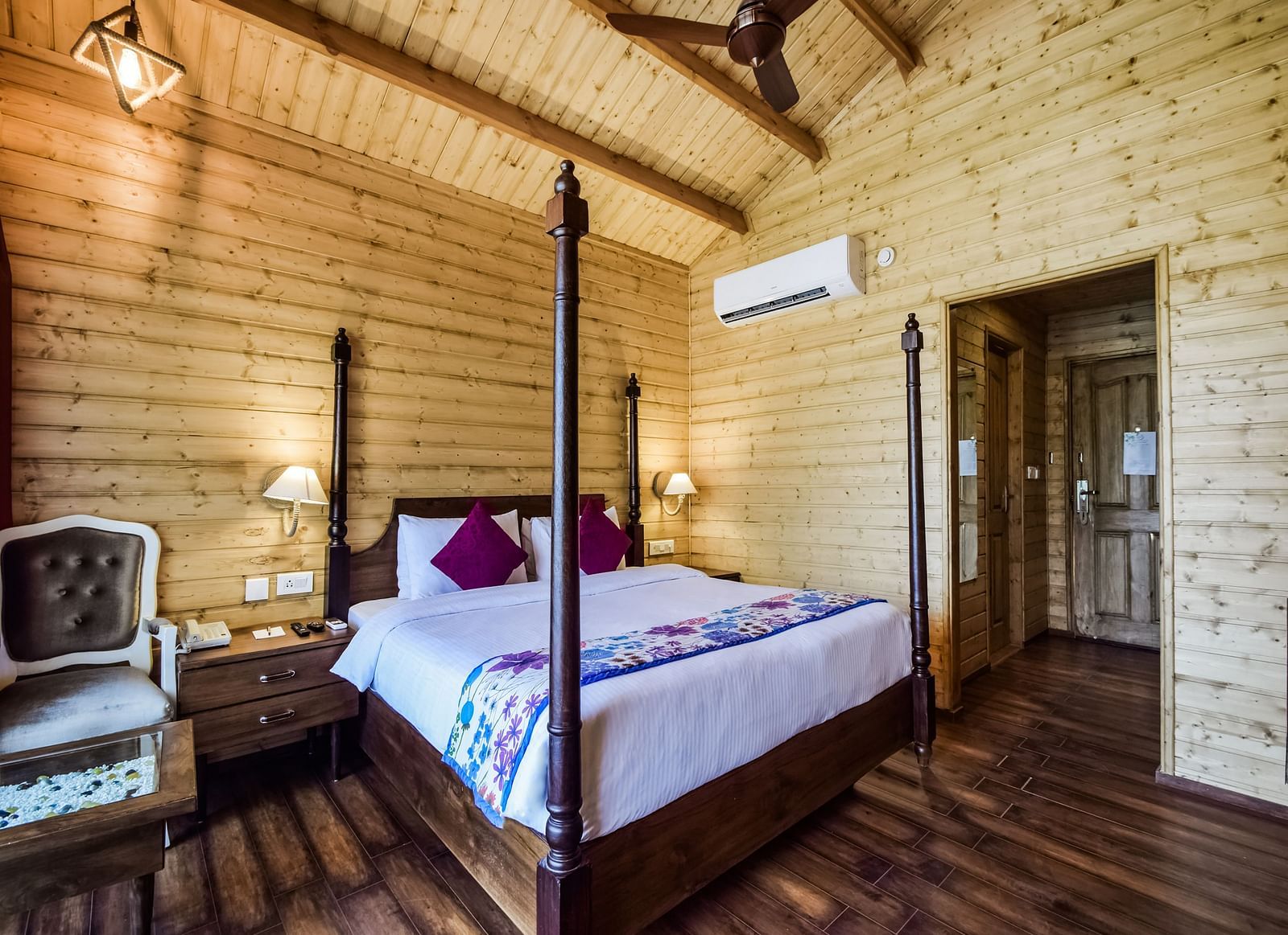 A hotel room with wooden walls, a bed with pillows on it and a chair.- Bamboo Saa Resort & Spa, Udaipur