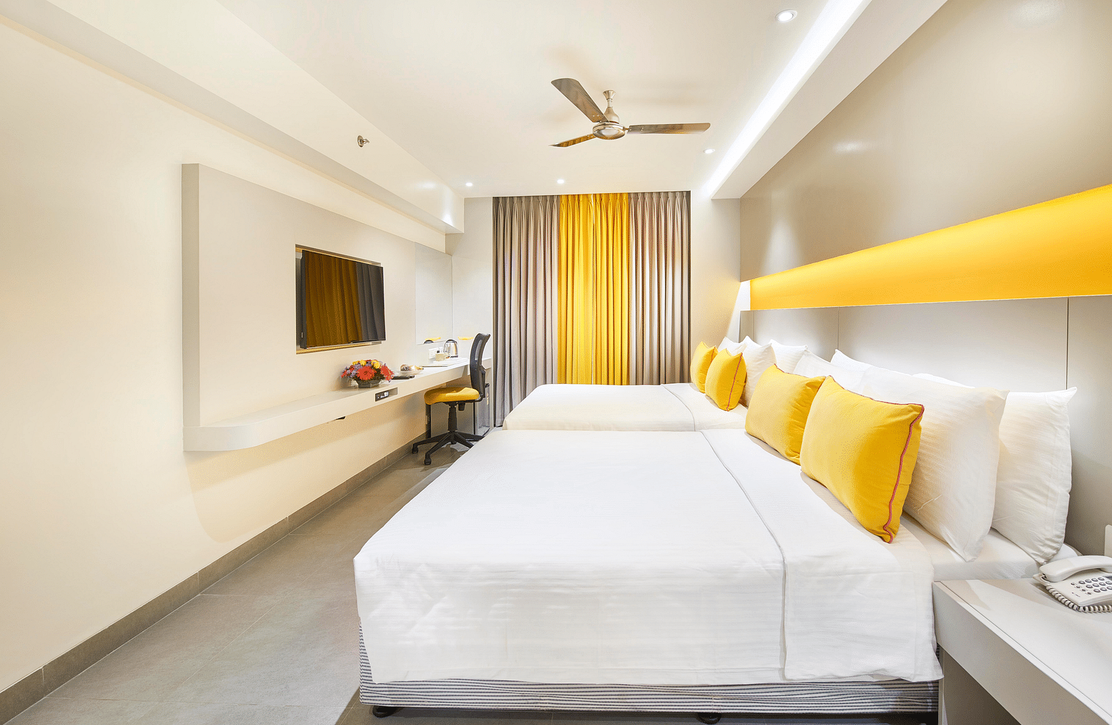  The spacious room has a large bed, a single loveseat beside the bedside table, a wall-mounted television across from it, and a window to the side covered with a curtain