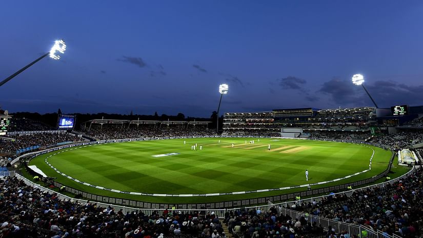 a far out view of a cricket stadium with floodlights on and dark skies in the background