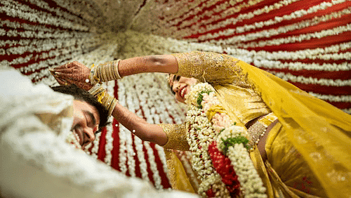Bride in yellow lehenga during traditional Indian wedding ceremony, lying under vibrant floral canopy with festive vibes.