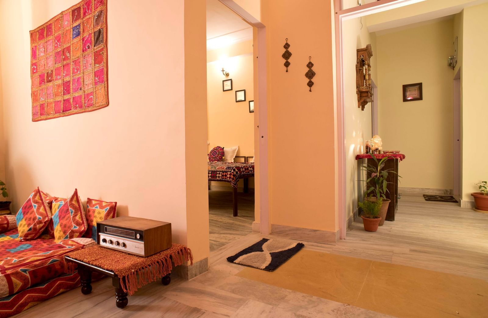 A hallway with potted plants, wall art, and a visible dining space with chairs and table in the background at Jaypore360 Homestay in Jaipur.