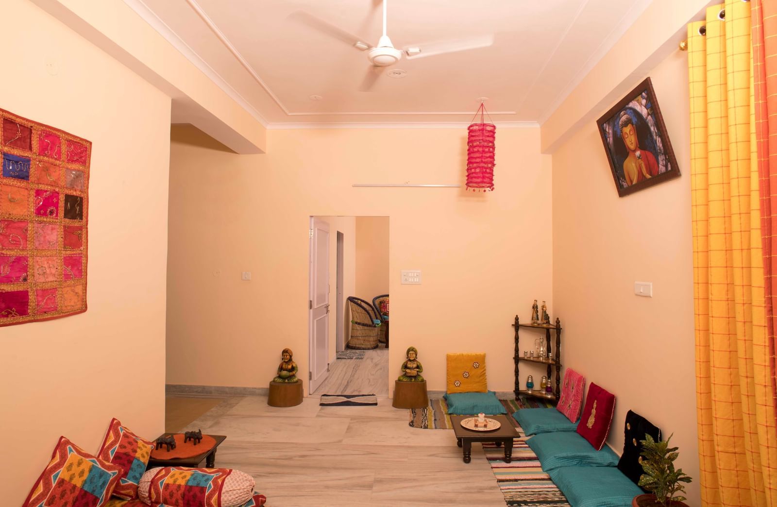 A room with floor cushions, wall art, low table, and decorative items arranged against the walls at Jaypore360 Homestay in Jaipur.