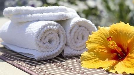 A yellow hisbiscus flower on a table along with freshly folded white towels.