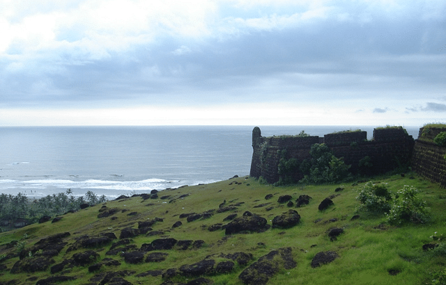 An image of Chapora fort from where a river can be seen and on the adjacent side there is a steep hill with grass and plants