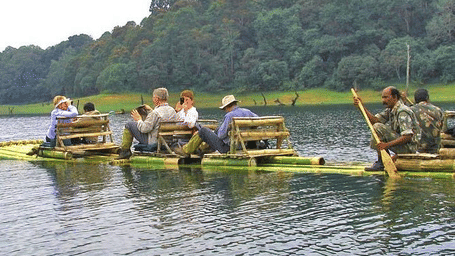 A group of visitors paddling traditional boats on a calm lake bordered by thick forest cover.