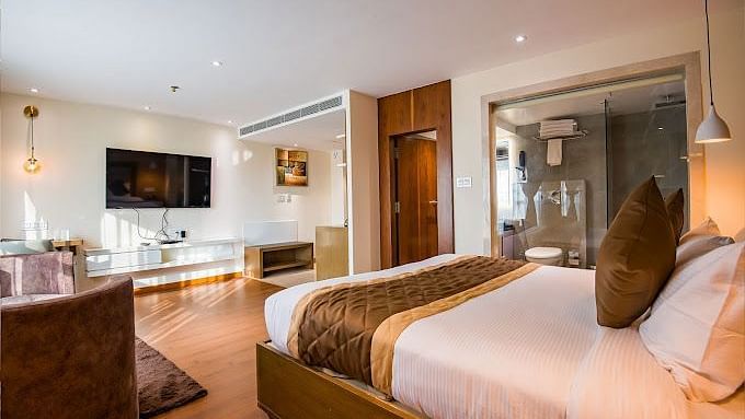 A premium hotel room with a large bed, a wooden table to the side, a wall-mounted television, and a few fancy lamps around the room at Yashshree The Imperial Inn, Siliguri.